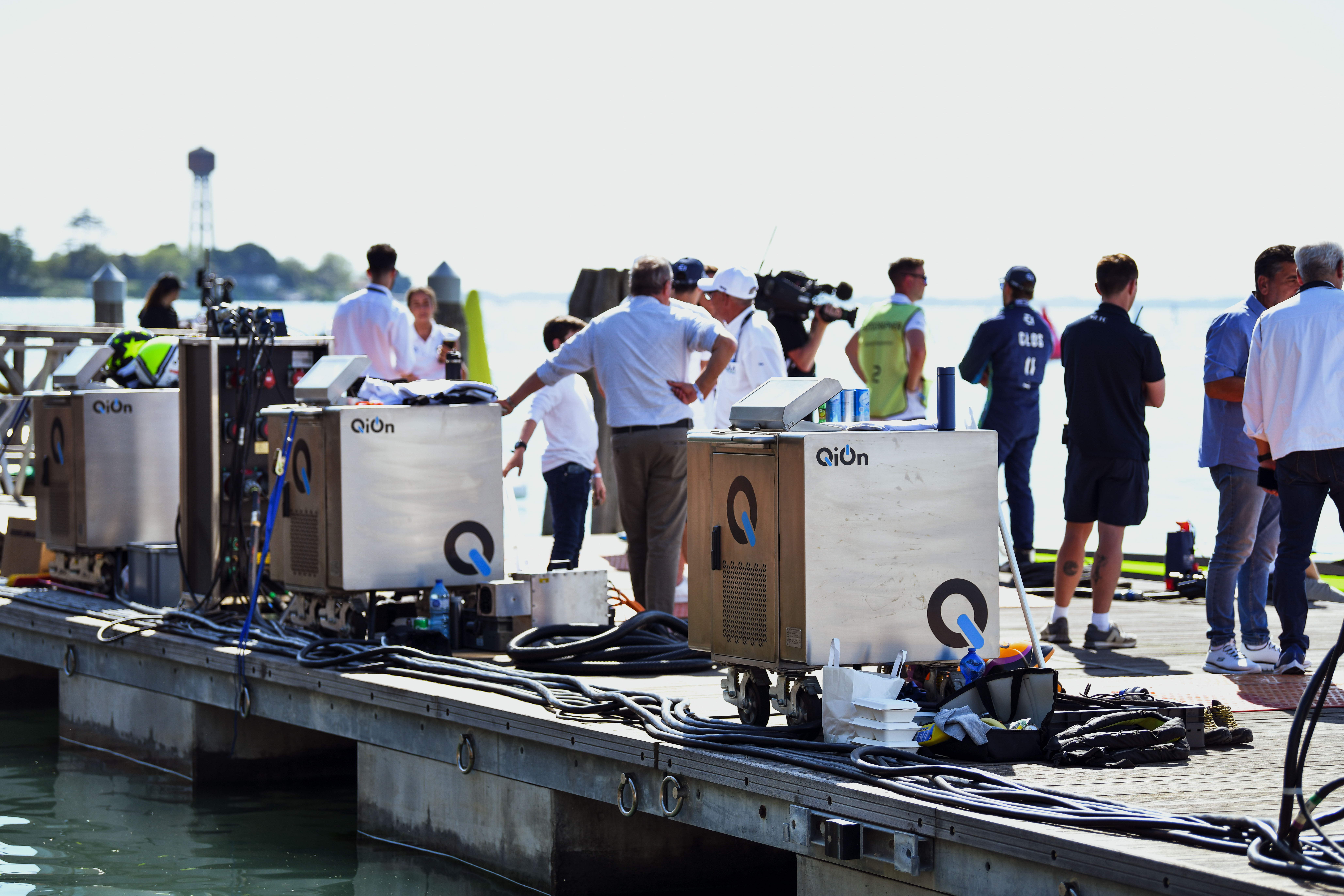QiOn charging units deployed on a wooden race dock at a UIM E1 Series electric powerboat racing event, with crew and camera teams surrounding the marine-grade chargers