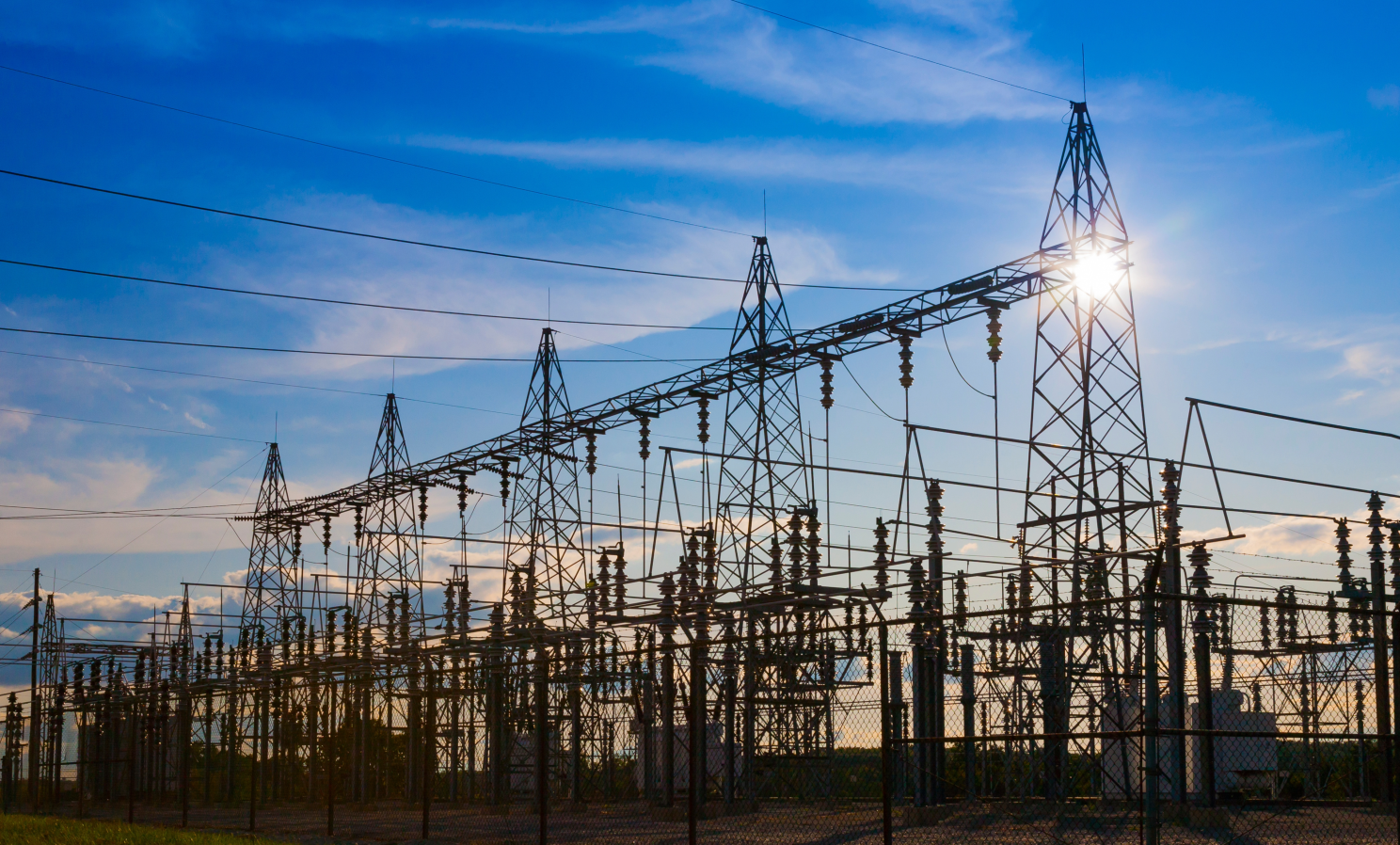 High-voltage electric power substation with transmission towers at sunset, representing grid infrastructure where BESS systems and Virtual Power Plants provide ancillary services and energy flexibility